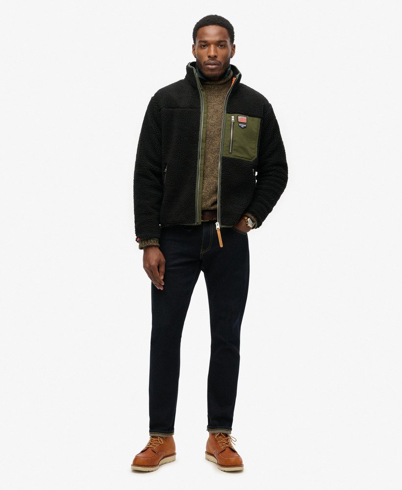 Man wearing a black jacket with a green inner lining, dark pants, and brown boots on a white background