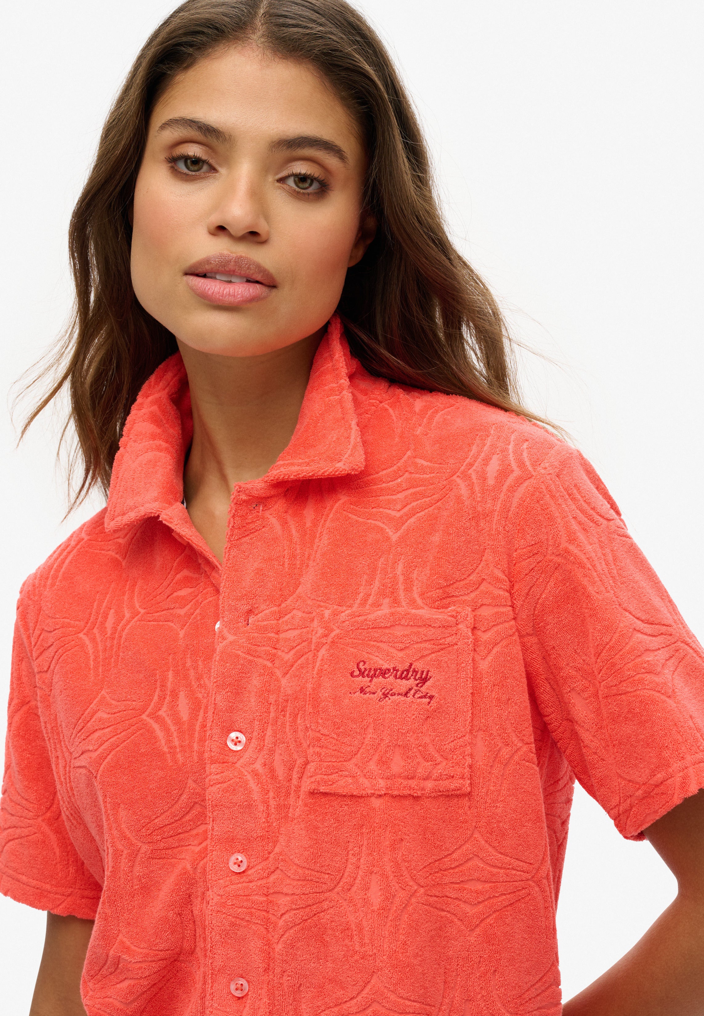 Woman wearing a coral patterned shirt with a Superdry logo on a white background